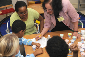 Dr. Toby Horn (right) demonstrates how to string A T C G beads in the order of a specific genome sequence.