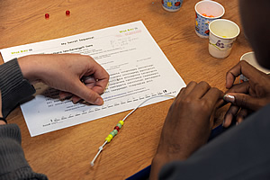 A Children's Inn guest uses Dr. Horn's guide for stringing each bead in a specific genomic sequence.